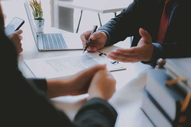 Homeowners review insurance documents beside a house model, roof samples, and a household inventory checklist.